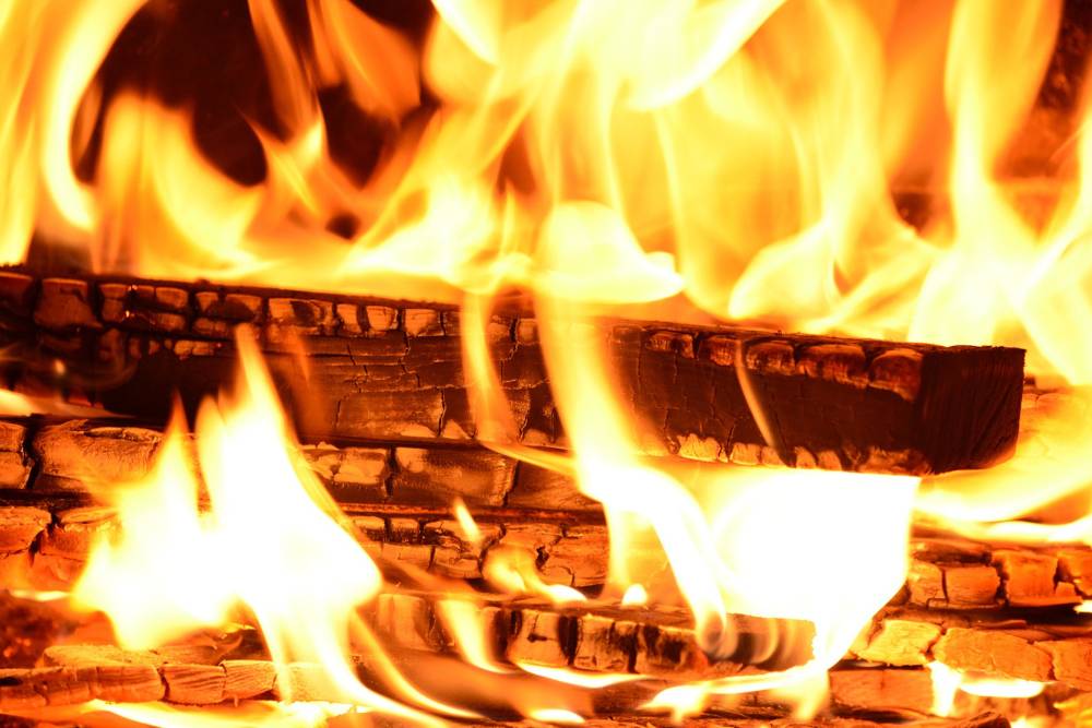A roaring orange fire burns a pile of partially ashen, split wood.